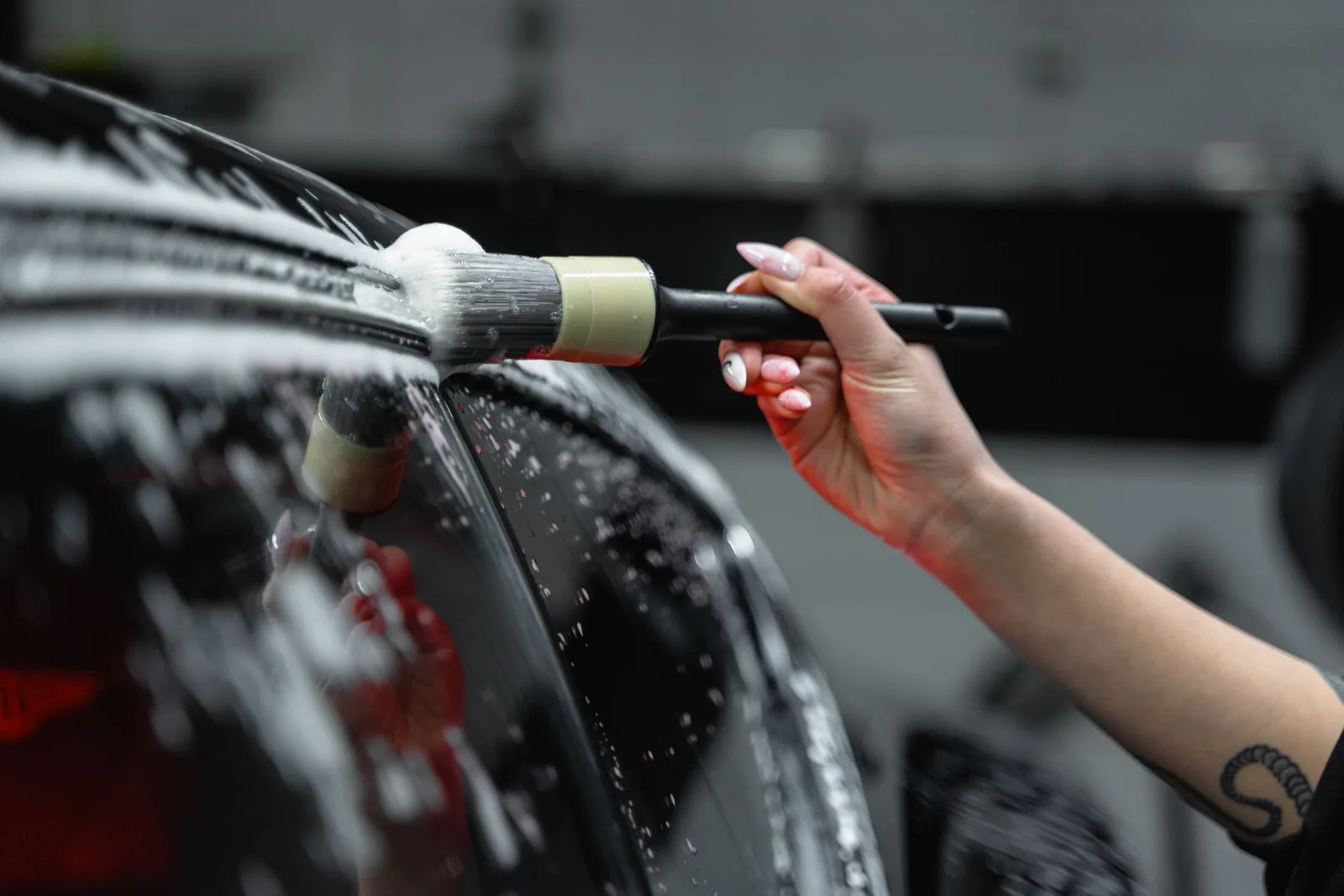 Hand cleaning car exterior with brush and foam