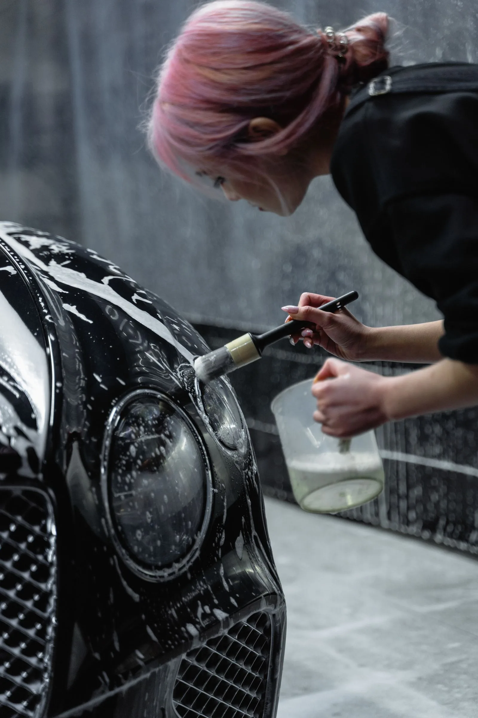 Cleaning a car headlight with brush and soap at a detailing service