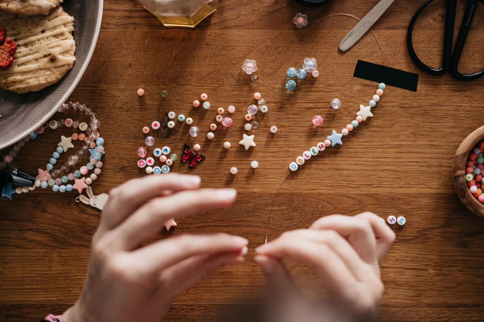 Hands crafting personalized jewelry with beads at a wooden table