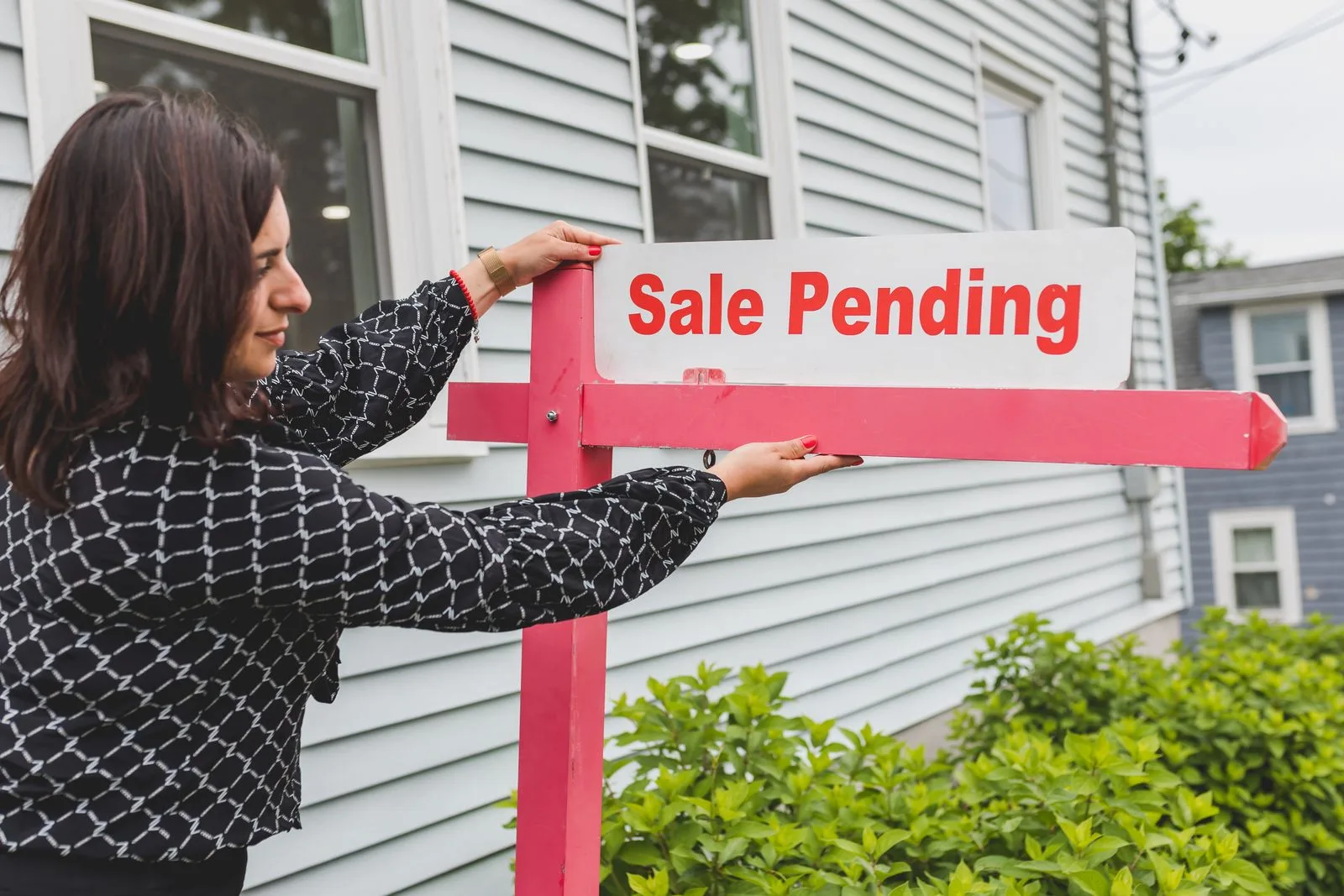 A realtor adjusting a sale pending sign outside a house