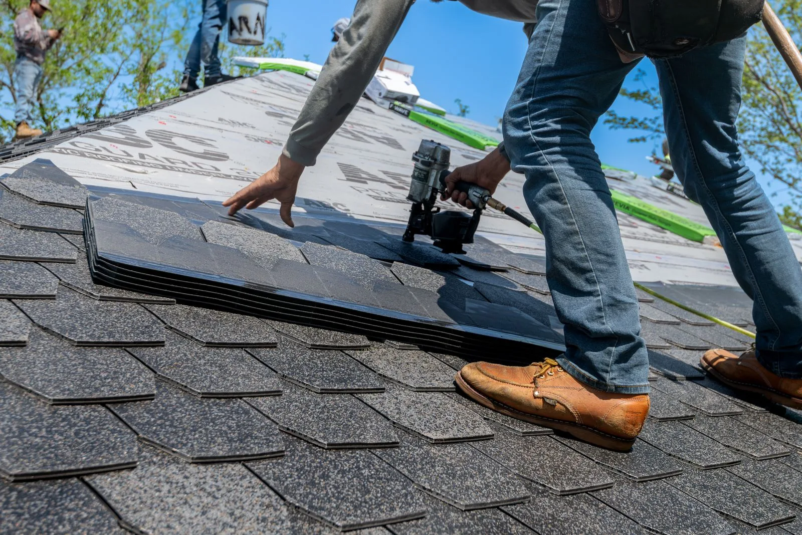 Roofer using a nail gun for shingle installation on a residential roof