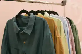 Row of colourful linen shirts hanging on black hangers from a clothing rail