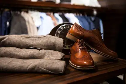 Brown leather brogue shoes beside a stack of folded grey sweaters in a clothing shop