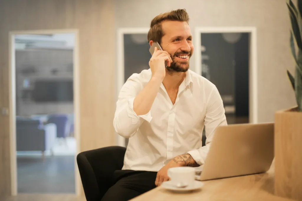Smiling man on a phone call at a laptop with a cup of coffee
