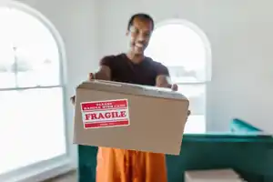 Smiling mover holding out a cardboard box with a Fragile handle with care label