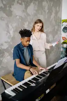 Music teacher holding sheet music while a student plays a digital piano