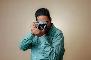 Photographer in a green striped shirt raising a vintage Canon film camera to frame a shot