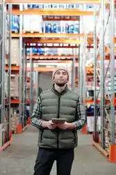 Parts and stock manager holding a tablet in a warehouse aisle between tall shelving
